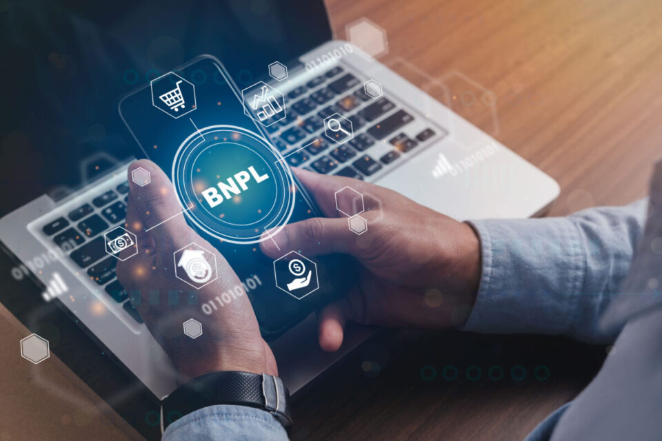 A person using his mobile phone over a laptop to illustrate the concept of BNPL (Buy Now, Pay Later) shopping