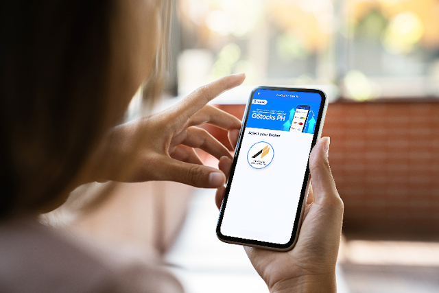 A woman holding a mobile phone with the GStocksPH app