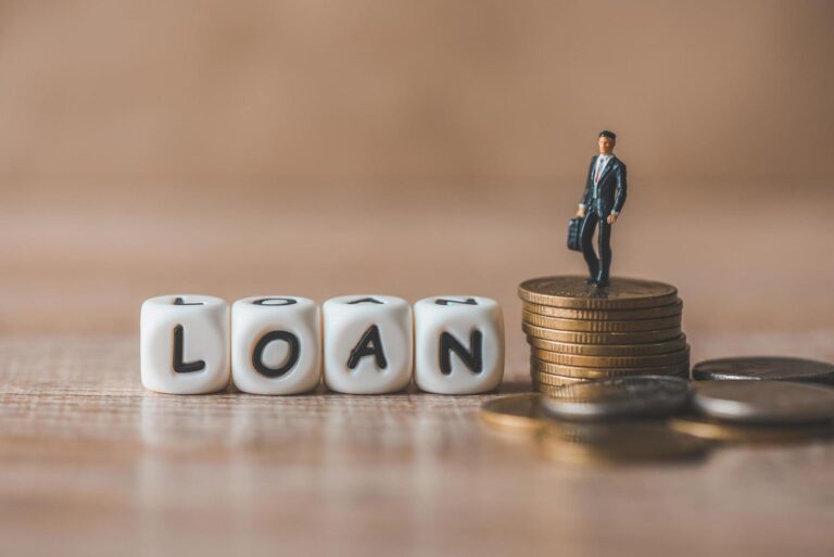 Dice forming the word LOAN, and a miniature bank official standing on a heap of coins
