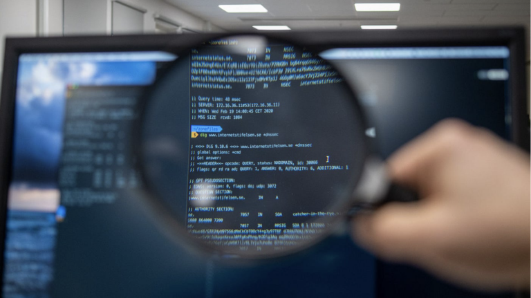 A cybercrime expert is shown here while using a magnifying glass on his laptop to solve cybersecurity concerns