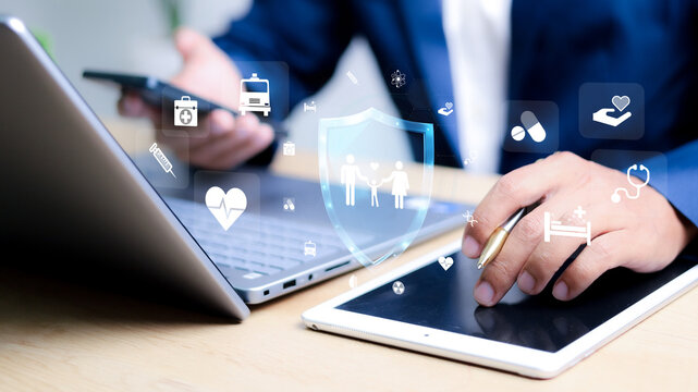 The importance of InsurTech as shown in this photo of a business professional using a tablet and laptop, with floating digital healthcare and insurance icons in the background