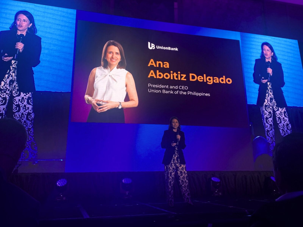 Ana Aboitiz Delgado, President and CEO of UnionBank of the Philippines, speaking on stage at a corporate event with a large screen behind her displaying her name, title, and photo.