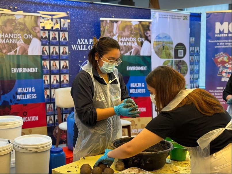 Two women wearing gloves and aprons, working with what appears to be a dark, muddy mixture to make "Bokashi Balls as part of AXA Philippines' CSR program