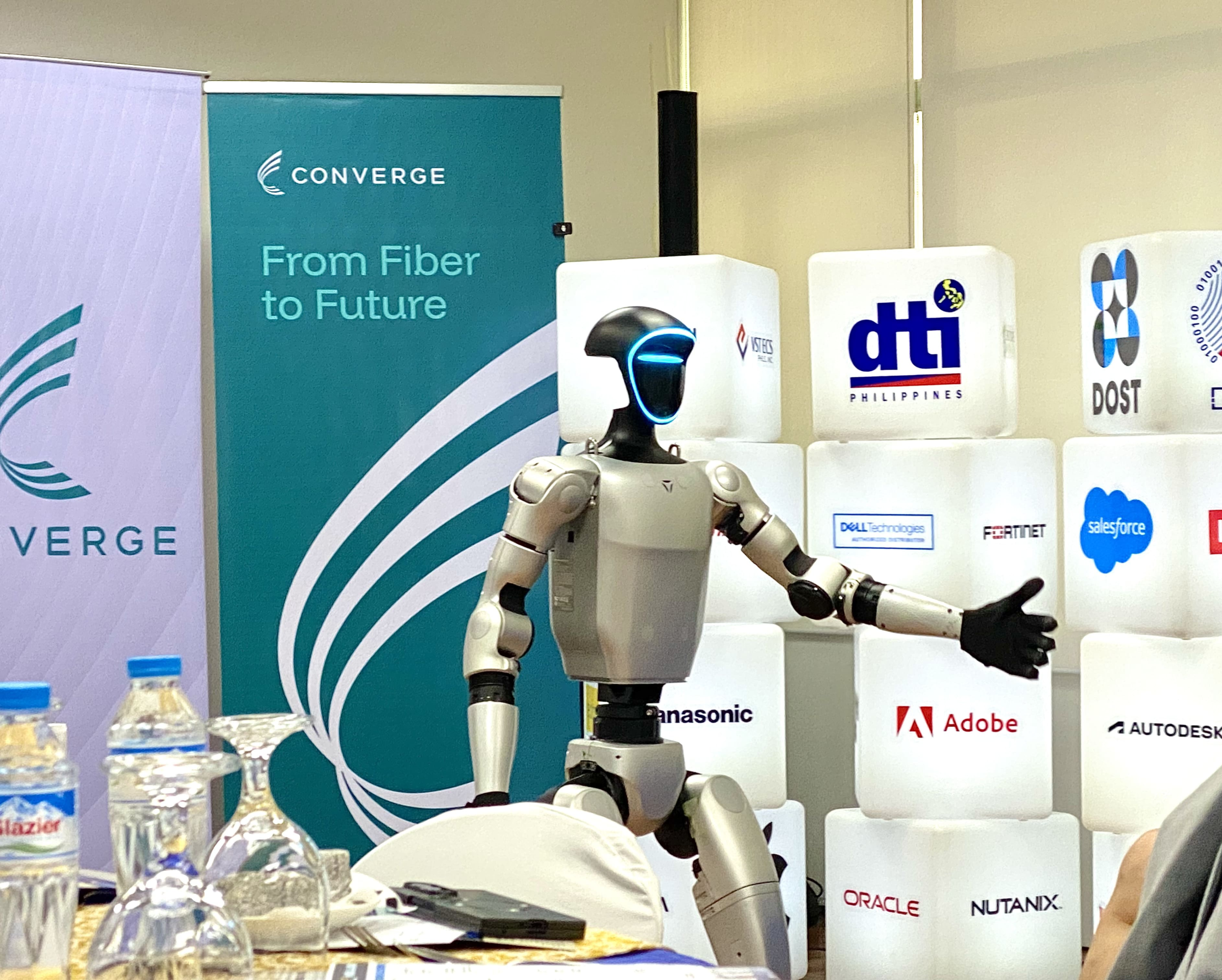A humanoid robot waving at the audience during 51st Philippine Business Conference & Expo media launch, symbolizing the role of technology and digital transformation, with Converge with PCCI and DTI banners in the background.