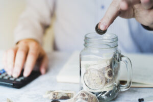 A hand putting coins inside a jar is used to illustrate top savings accounts in 2025 that offers the best interest rates