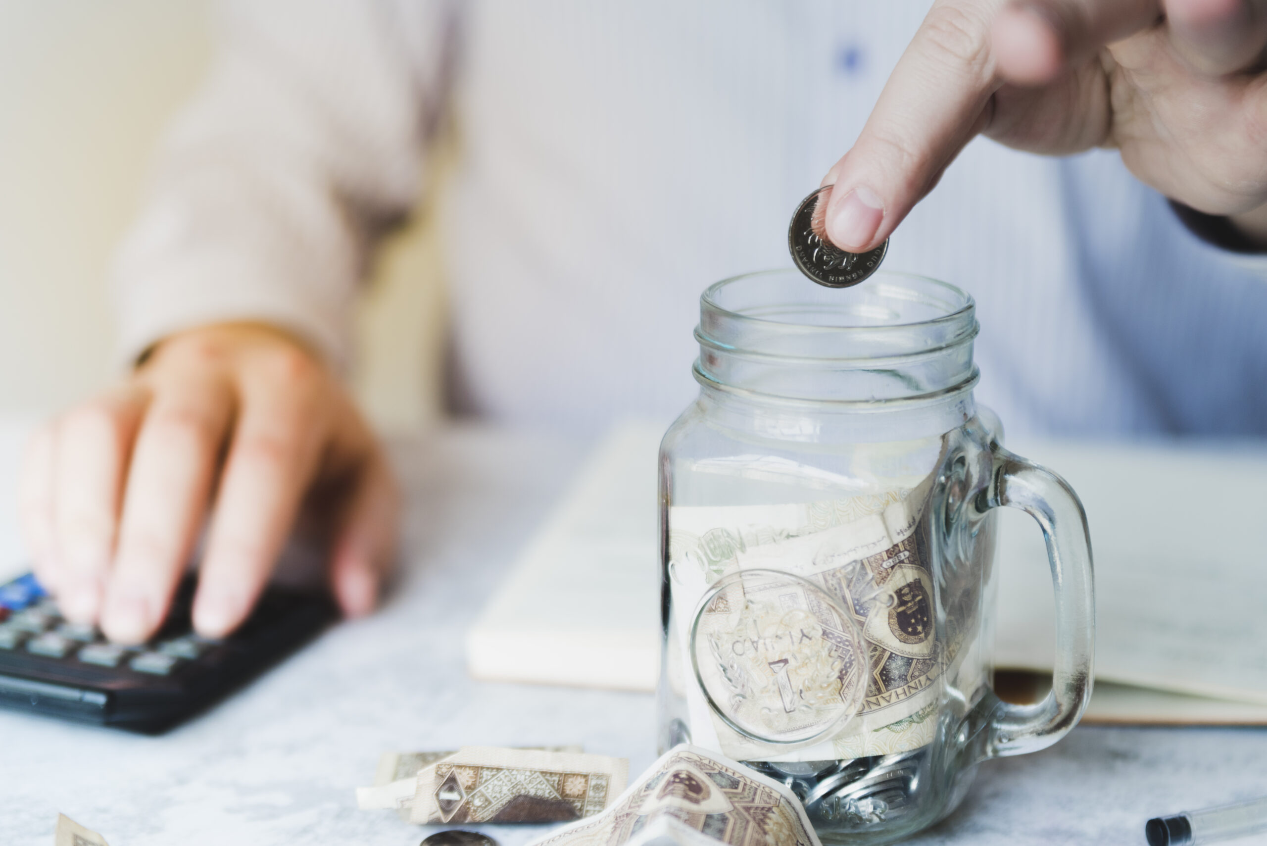 A hand putting coins inside a jar is used to illustrate top savings accounts in 2025 that offers the best interest rates