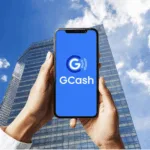 A man holds up his mobile phone amidst tall buildings in the background as GCash delays IPO to 2026 amid market volatility