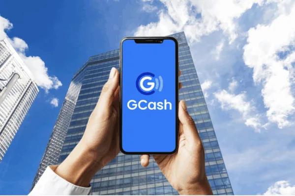 A man holds up his mobile phone amidst tall buildings in the background as GCash delays IPO to 2026 amid market volatility