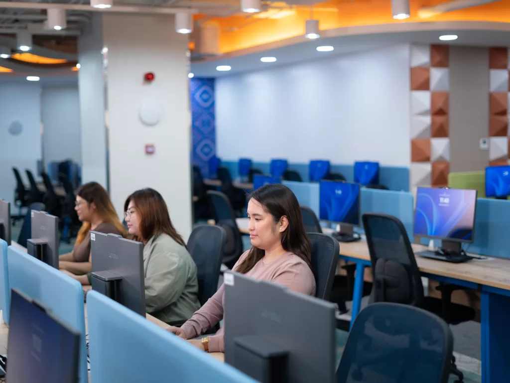 Employees working at their desks inside the newly launched TaskUs Hiraya site in Las Piñas, featuring a modern workspace with computers, bright lighting, and colorful interiors.