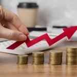 A hand holding arrow over coins to show how inflation is seen to stay within target range