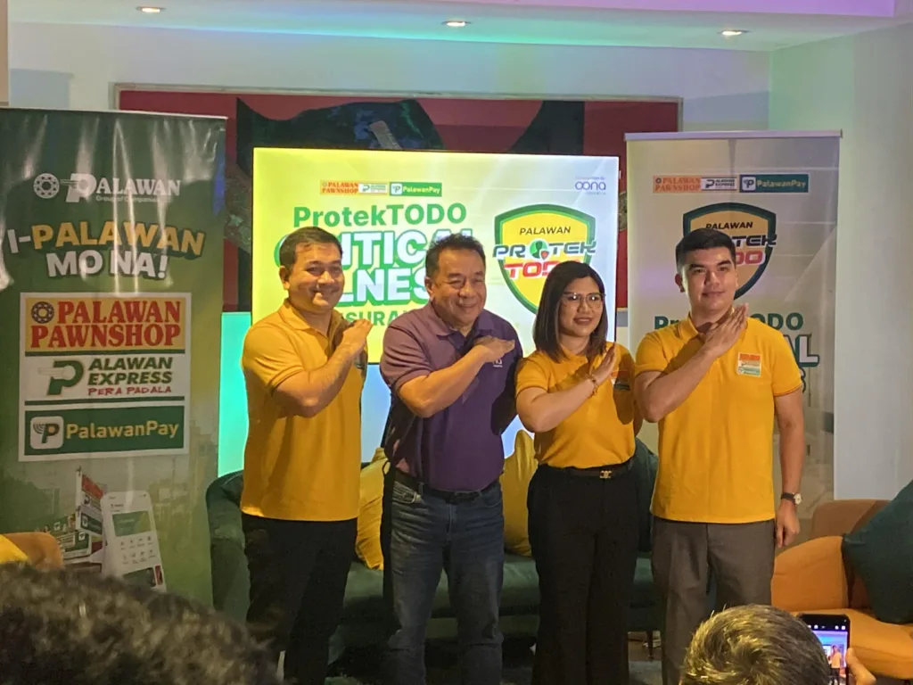 Four company representatives stand side by side on a small indoor stage during a Palawan Group of Companies brand event, posing with a synchronized hand-over-chest gesture. Three individuals wear yellow Palawan-branded polo shirts, while one wears a purple polo shirt, all smiling toward the camera. Behind them are prominent banners and a digital display with clearly visible text: “I-Palawan Mo Na!”, “Palawan Pawnshop,” “Palawan Express Pera Padala,” “PalawanPay,” and “ProtekTODO Critical Illness Insurance,” along with the shield-shaped “Palawan ProtekTODO” logo and “Underwritten by Oona Insurance.” The setting features warm lighting and corporate décor, emphasizing unity, trust, and brand promotion related to insurance, financial services, and customer protection in the Philippines.