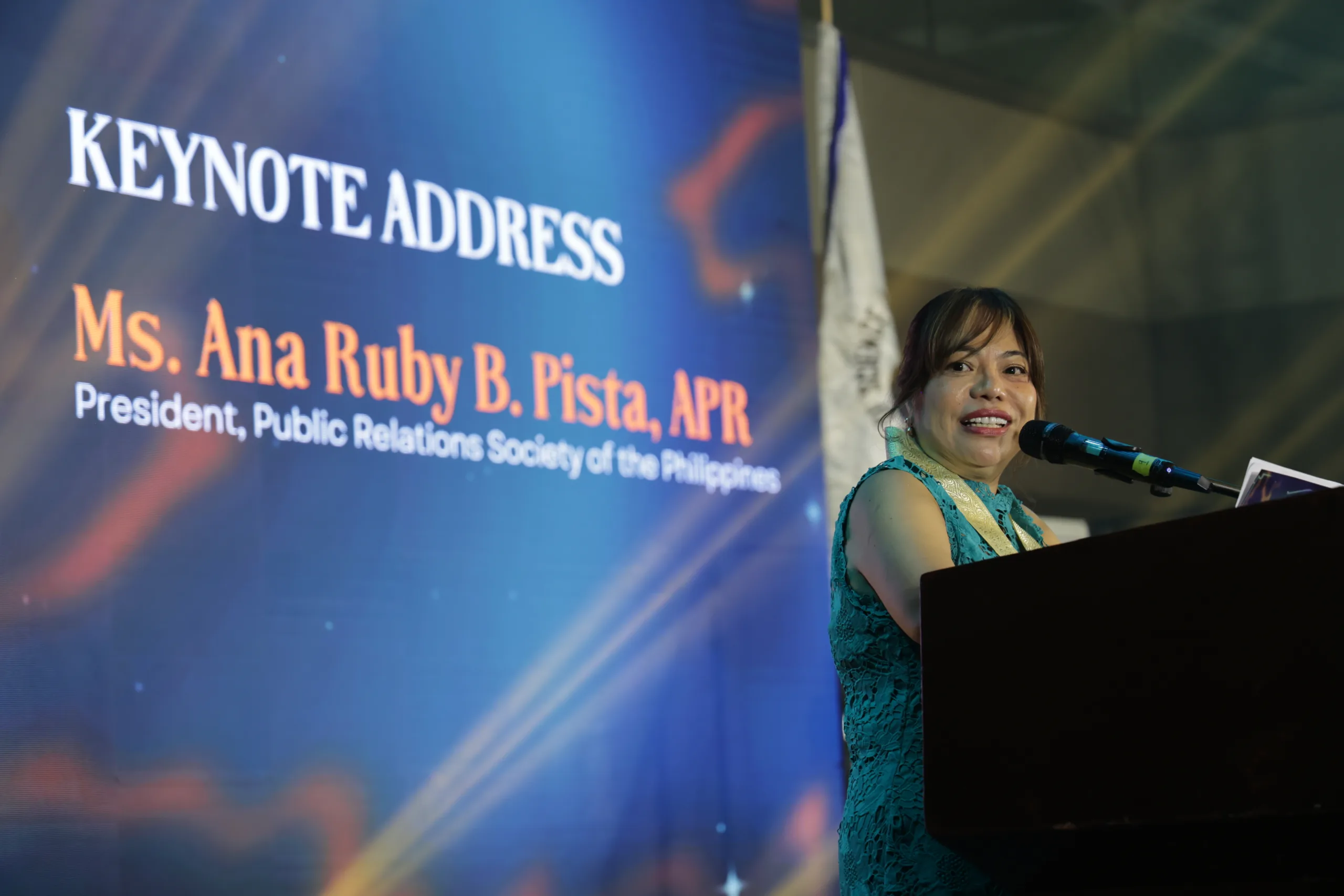 PRSP President Ana Ruby B. Pista delivers a keynote address at DOST-TAPI’s 39th anniversary celebration, speaking at a podium with a backdrop displaying her name and title as President of the Public Relations Society of the Philippines.
