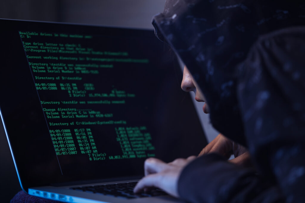 computer hacker hooded shirt typing software algorithms stealing data from computer network laptop