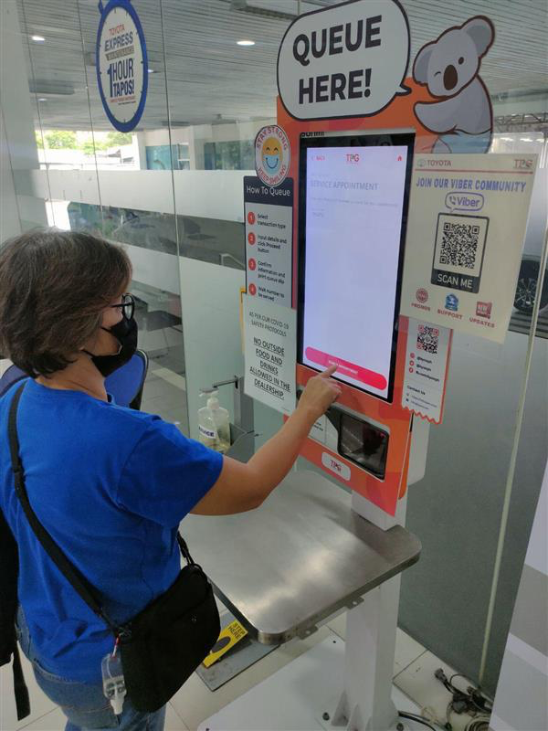 A customer uses a Kyoo touchscreen queueing kiosk at an automotive service center.